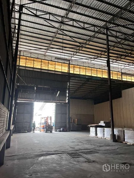 Warehouse for rent in Rat Burana, Bangkok - Spacious warehouse interior with high steel truss roof, wide loading door and concrete floor.