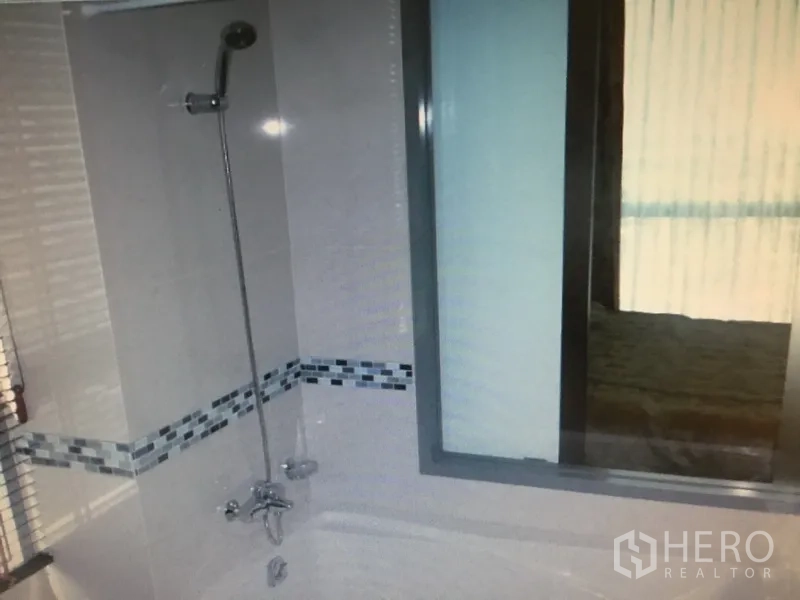Condominium for rent in Ratchathewi, Bangkok - Bathroom with shower over bathtub, white tiles and mosaic trim, and a window to the bedroom.