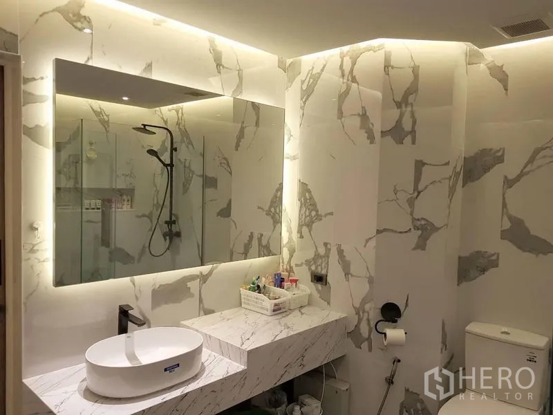 Condominium for rent in Bang Rak, Bangkok - Bathroom vanity with backlit mirror, vessel sink and marble-patterned walls.