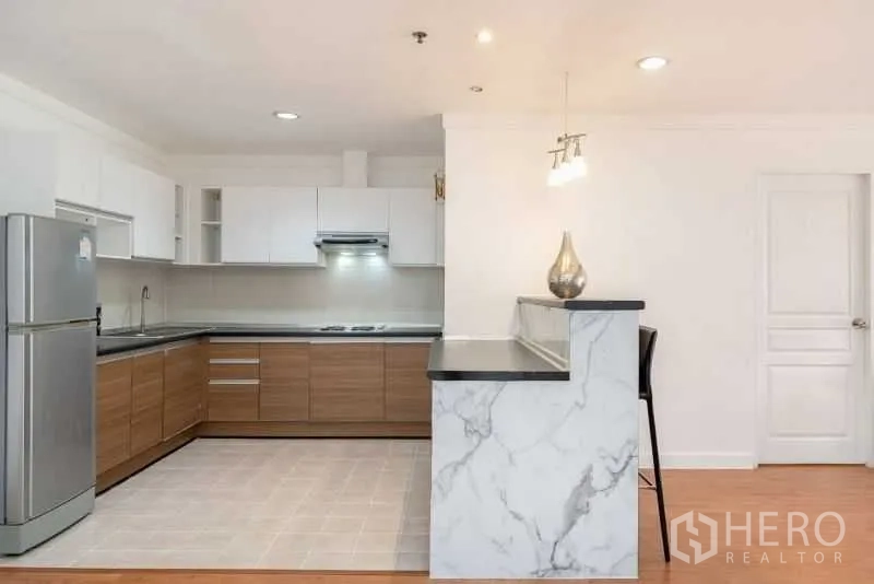 公寓 出租在Khlong Toei, Bangkok - 现代L型厨房，白色橱柜、灶台与抽油烟机，配大理石吧台和高脚椅。