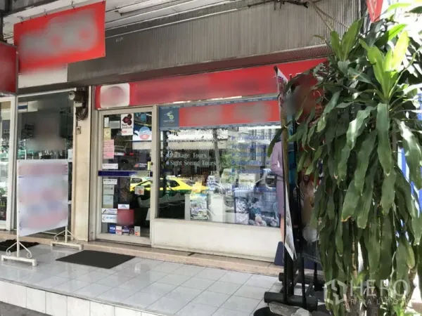 零售空间 出租在Watthana, Bangkok - 街边商铺门面，玻璃立面与红色招牌，瓷砖入口及带遮棚的人行道，靠近BTS阿索克站。