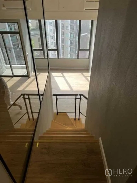 Condominium for sale in Huai Khwang, Bangkok - Staircase view down to the double-height living room and large windows.