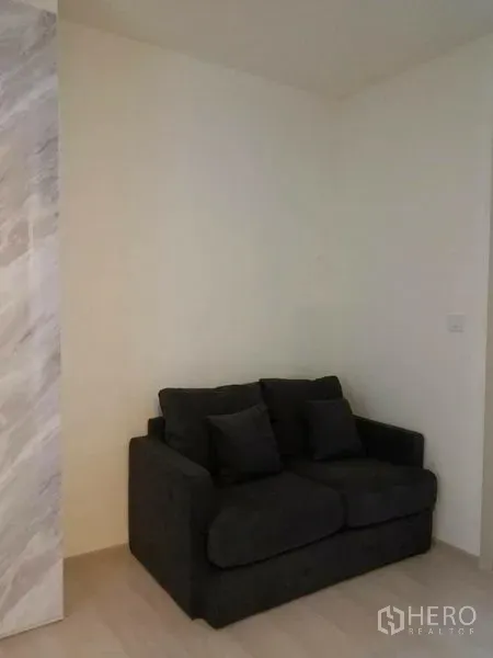 คอนโด ให้เช่าในDin Daeng, Bangkok - มุมนั่งเล่นโซฟาสีเข้มสองที่นั่ง ผนังสีอ่อน พื้นไม้