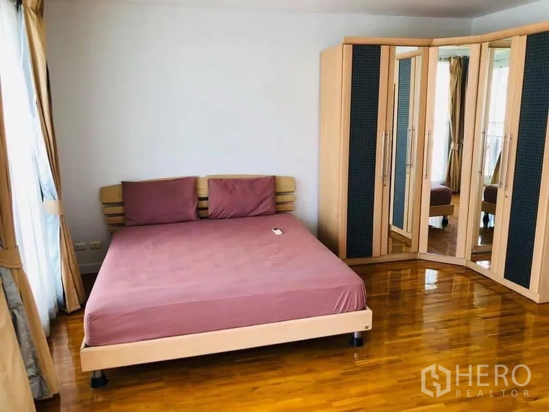 Townhouse for rent in Khlong Toei, Bangkok - Corner primary bedroom with mirrored wardrobe and polished wooden flooring.