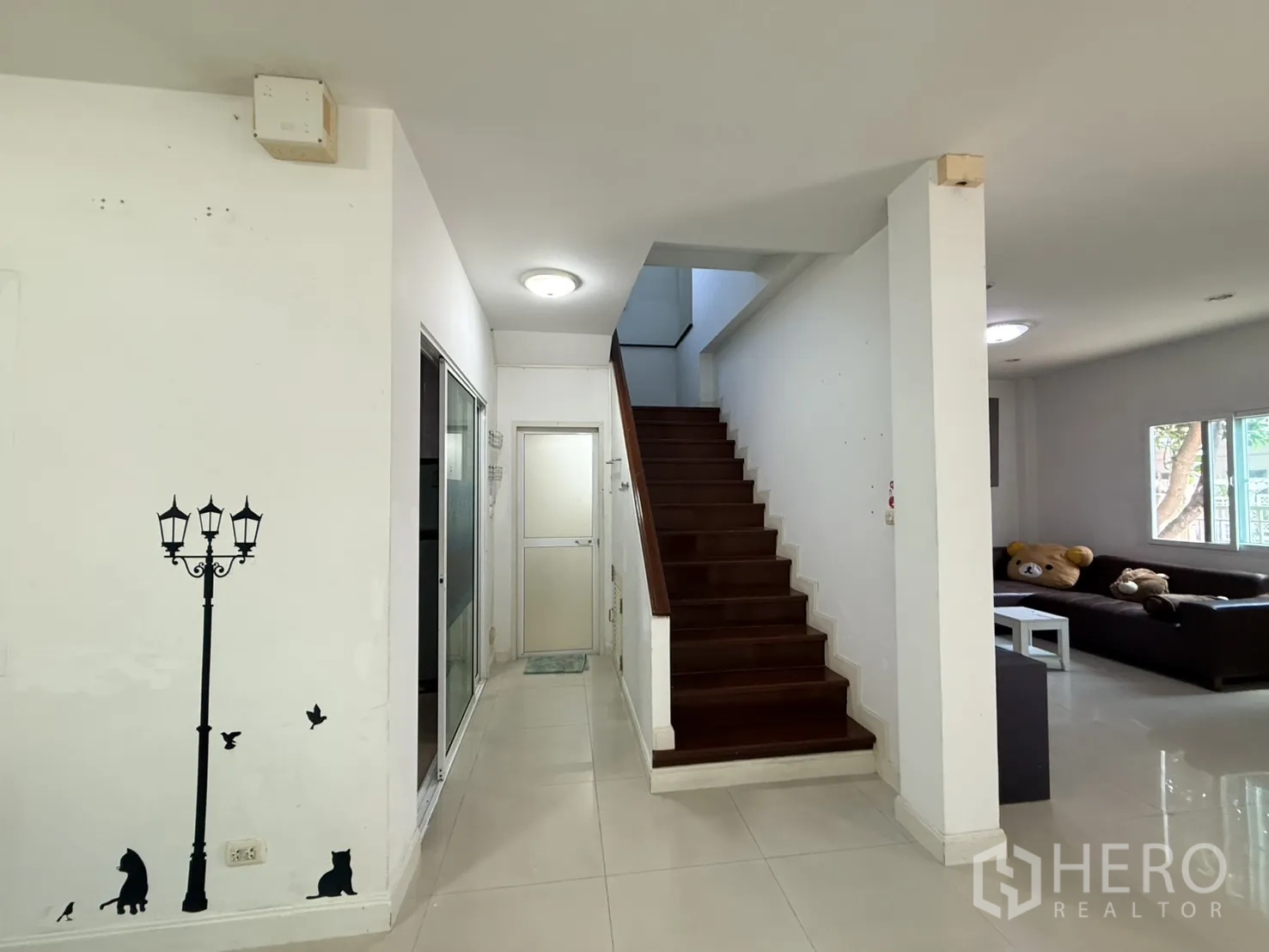 Detached House for rent in Lam Luk Ka, Pathum Thani - Interior hallway with wooden staircase and sliding door off the living area.