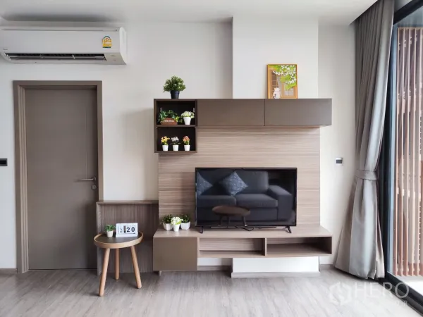 Condominium for rent in Watthana, Bangkok - TV feature wall with built-in shelves, air conditioner, and curtains in a modern condo.