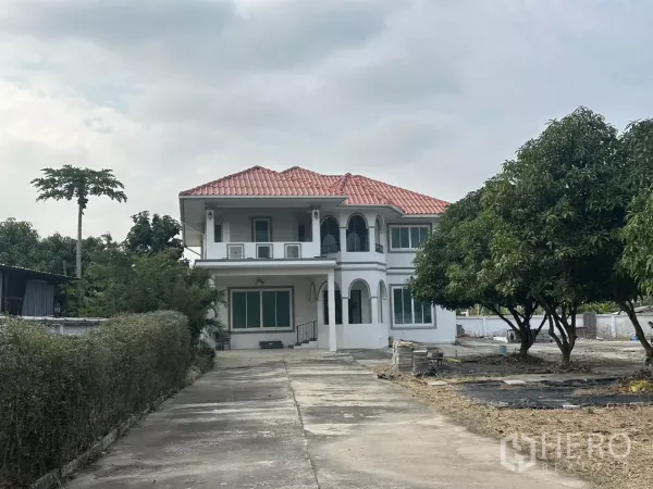 สำนักงานที่บ้าน ให้เช่า - มุมมองด้านหน้าบ้านสองชั้นหลังคากระเบื้องสีแดง ถนนทางเข้ายาวและมีต้นไม้ใหญ่.