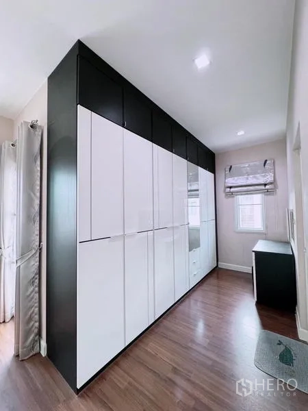Detached House for rent in Prawet, Bangkok - Walk-in wardrobe corridor with tall white cabinets and wood flooring.