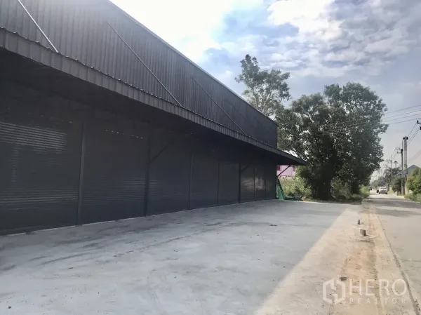 คลังสินค้า ให้เช่าในLam Luk Ka, Pathum Thani - ด้านหน้าทอดยาวของโกดังมีกันสาดและทางเข้าออกกว้างมีต้นไม้ข้างทาง