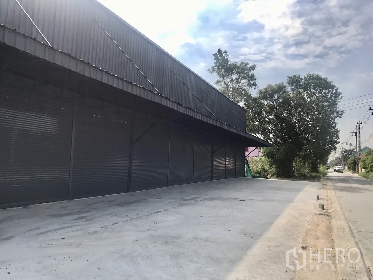 คลังสินค้า ให้เช่าในLam Luk Ka, Pathum Thani - ด้านหน้าทอดยาวของโกดังมีกันสาดและทางเข้าออกกว้างมีต้นไม้ข้างทาง