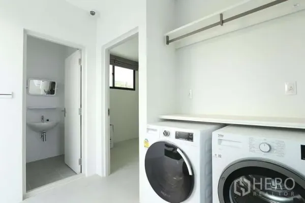 บ้าน ให้เช่าในSaphan Sung, Bangkok - ห้องซักรีดสว่างพร้อมเครื่องซักผ้าและอบผ้าแบบฝาหน้า มีชั้นวางและประตูไปห้องน้ำขนาดกะทัดรัด