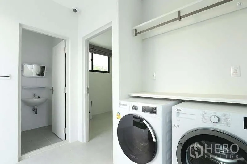 บ้าน ให้เช่าในSaphan Sung, Bangkok - ห้องซักรีดสว่างพร้อมเครื่องซักผ้าและอบผ้าแบบฝาหน้า มีชั้นวางและประตูไปห้องน้ำขนาดกะทัดรัด