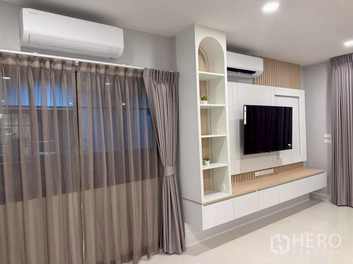 独立式住宅 出租在Bang Phli, Samut Prakan - 家庭活动区，媒体墙与悬空柜、置物架、大窗与空调采光良好。