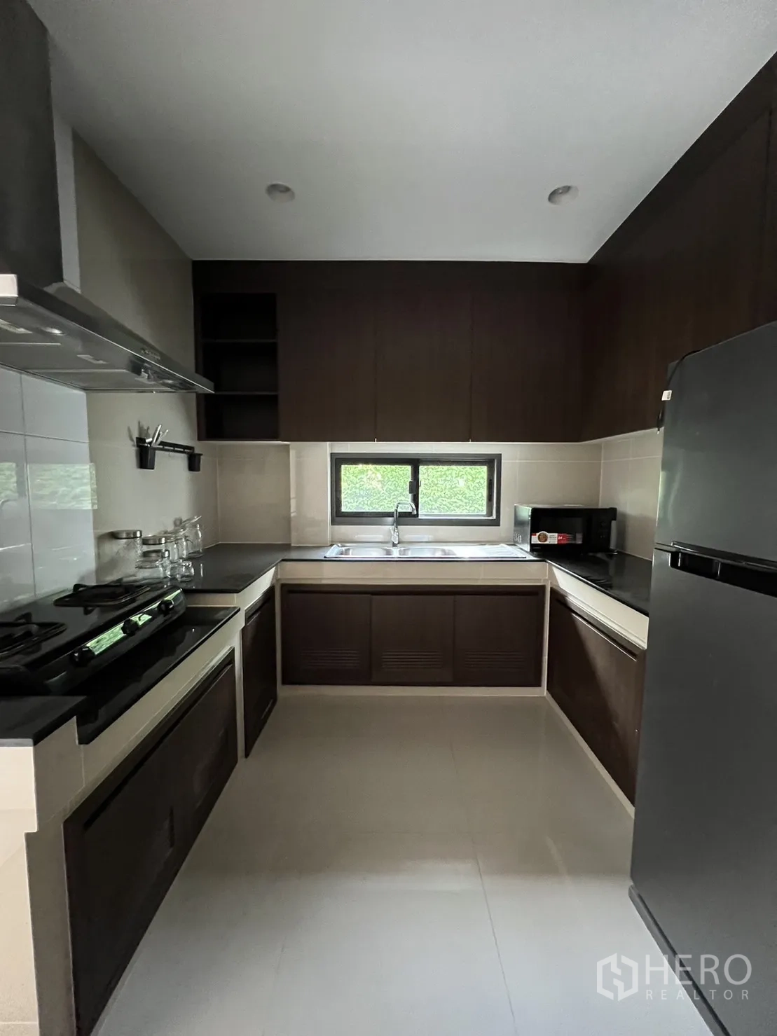 Detached House for rent or sale in Bang Kapi, Bangkok - Closed U-shaped kitchen with gas hob, dark cabinets and a window over the sink.