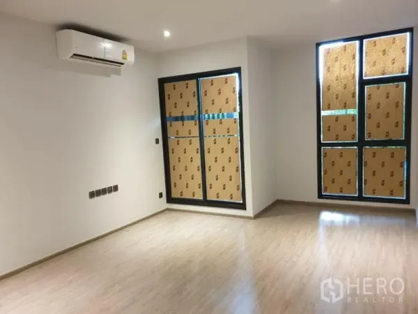 Condominium for sale in Watthana, Bangkok - Unfurnished living room with wood-look flooring, large windows and wall-mounted air conditioner.