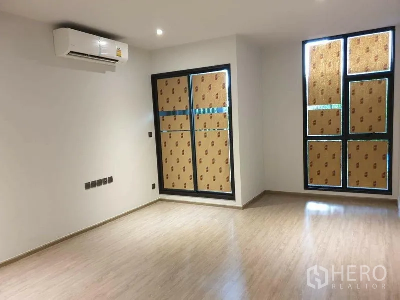 Condominium for sale in Watthana, Bangkok - Unfurnished living room with wood-look flooring, large windows and wall-mounted air conditioner.