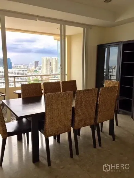 Condominium for rent in Watthana, Bangkok - Dining area with woven chairs opening to a balcony and wide Bangkok skyline view.