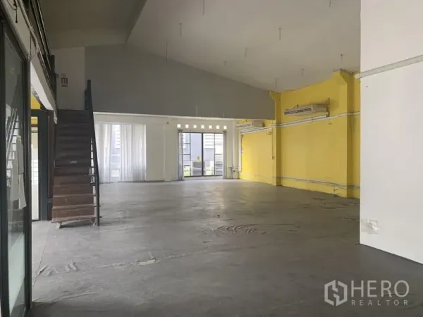 零售空间 出租在Khlong Toei, Bangkok - 宽敞零售楼层，黄色点缀墙，挑高天花，混凝土地面与后侧玻璃门。