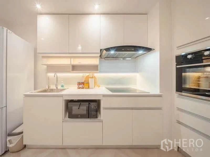 คอนโด ให้เช่า - ครัวสีขาวสมัยใหม่พร้อมเตาอินดักชัน เครื่องดูดควัน อ่างล้างจาน เตาอบคู่ และไมโครเวฟ