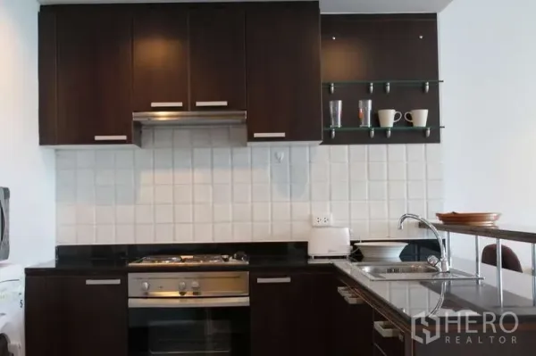 คอนโด ให้เช่าในSathon, Bangkok - ครัวยุคใหม่ตู้ไม้โทนเข้ม เตาและเตาอบ ผนังกระเบื้องสีขาว พร้อมชั้นกระจกวางแก้วและถ้วย