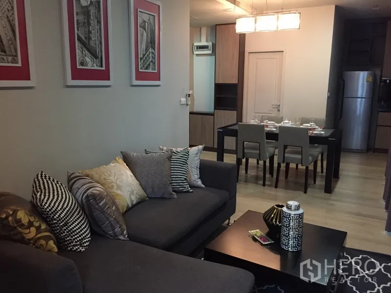 公寓 出租或出售在Bangkok - 开放式客厅，灰色转角沙发与装饰画，可望向餐区的现代公寓。