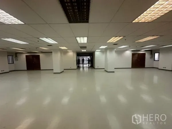 สำนักงาน ให้เช่าในPhaya Thai, Bangkok - พื้นที่สำนักงานโล่งกว้าง เพดานฝ้าทีบาร์พร้อมโคมไฟฟลูออเรสเซนต์ เสาสีขาว พื้นเรียบ และประตูกระจกด้านในสุด.