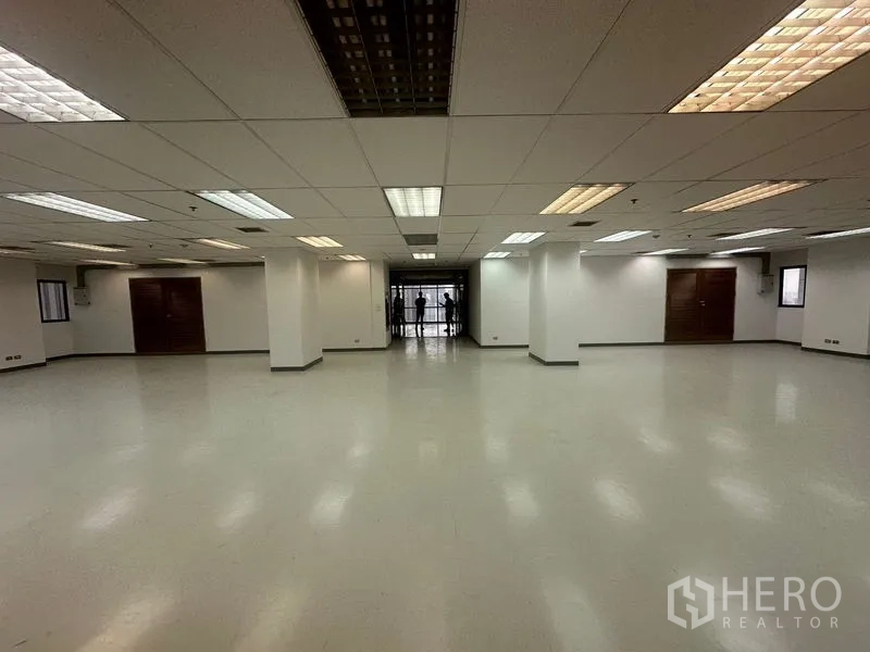 สำนักงาน ให้เช่าในPhaya Thai, Bangkok - พื้นที่สำนักงานโล่งกว้าง เพดานฝ้าทีบาร์พร้อมโคมไฟฟลูออเรสเซนต์ เสาสีขาว พื้นเรียบ และประตูกระจกด้านในสุด.