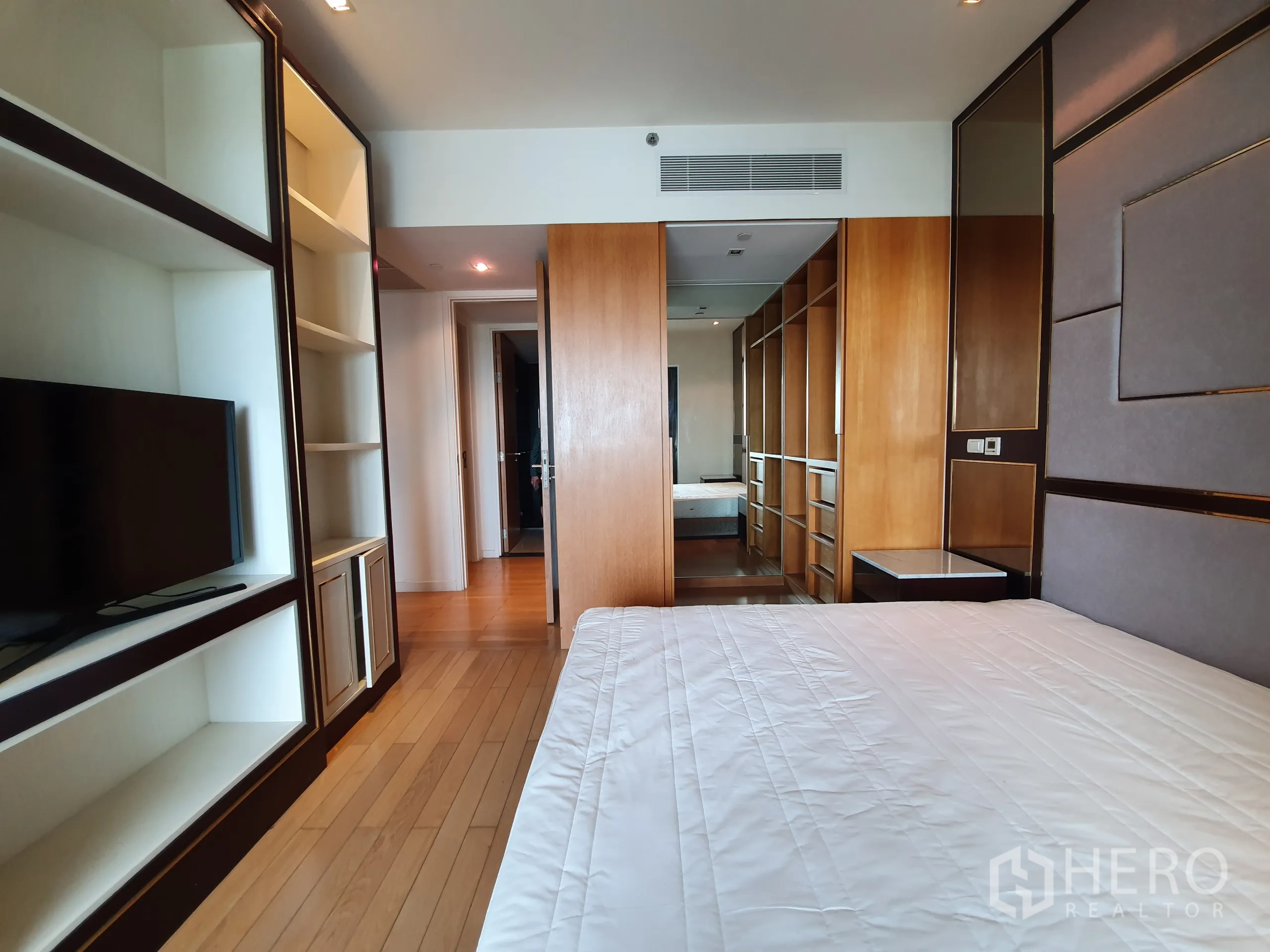 Condominium for rent or sale in Yan Nawa, Bangkok - Master bedroom with wood floors, built‑in shelving and TV, leading to a walk‑in closet.