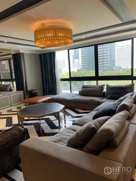 Condominium for rent or sale in Sathon, Bangkok - Luxury living room with sectional sofa, chandelier and city views through large windows in a Sathorn condo.