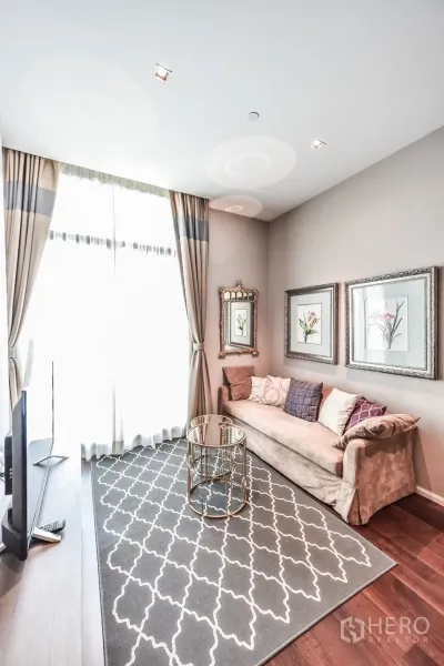 Condominium for rent or sale in Watthana, Bangkok - Bright living room with floor-to-ceiling curtains, patterned rug, gold round coffee table and framed botanical art.