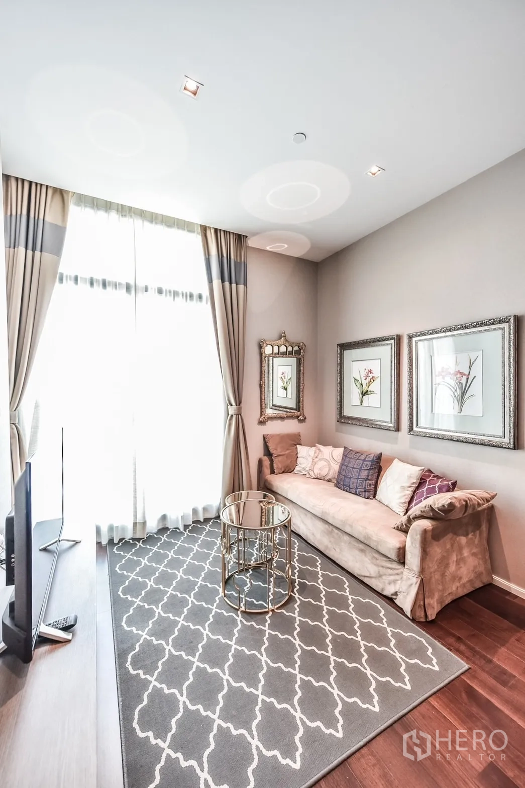 Condominium for rent or sale in Watthana, Bangkok - Bright living room with floor-to-ceiling curtains, patterned rug, gold round coffee table and framed botanical art.