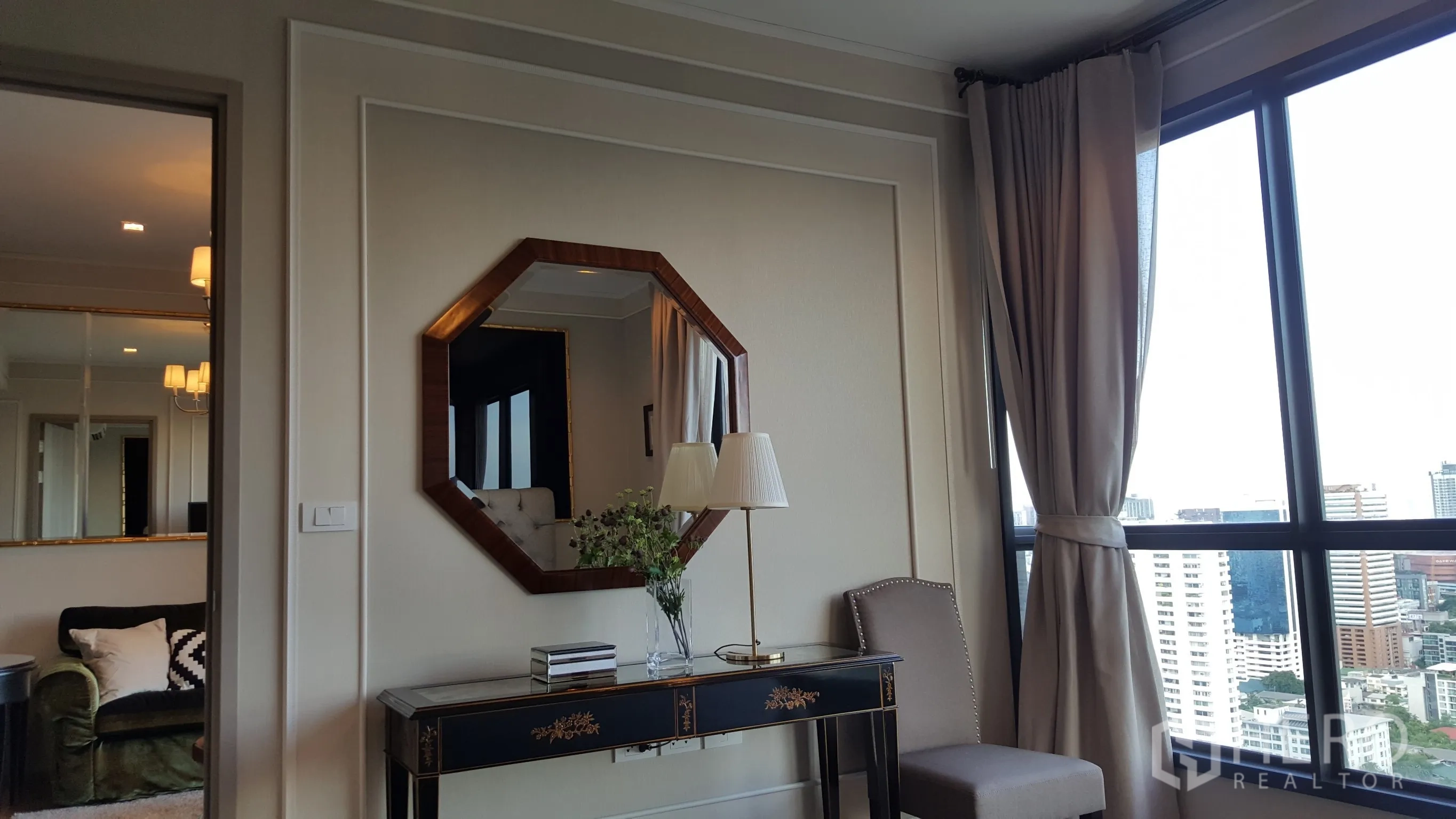 公寓 出租在Watthana, Bangkok - 优雅玄关桌与八边形镜子，旁有座椅与大窗，可观城市景色。