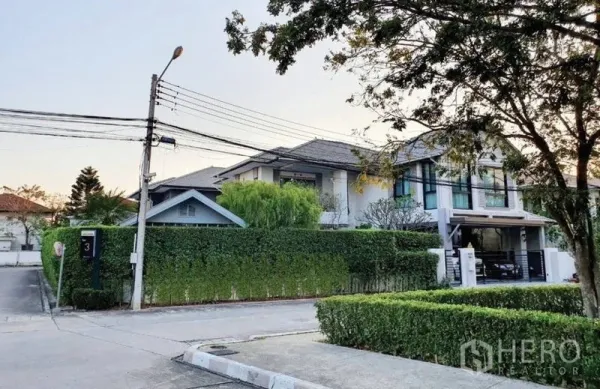 บ้าน ขายในLam Luk Ka, Pathum Thani - บ้านเดี่ยวสองชั้นบนแปลงมุม กำแพงต้นไม้เขียวขจี พร้อมที่จอดรถและถนนร่มรื่น.