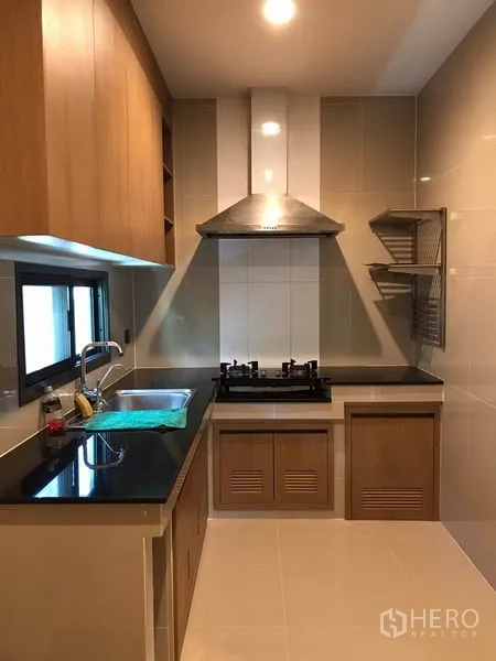 独立式住宅 出租在Bang Kapi, Bangkok - 封闭式厨房，黑色操作台、燃气灶与不锈钢抽油烟机、木质柜体。