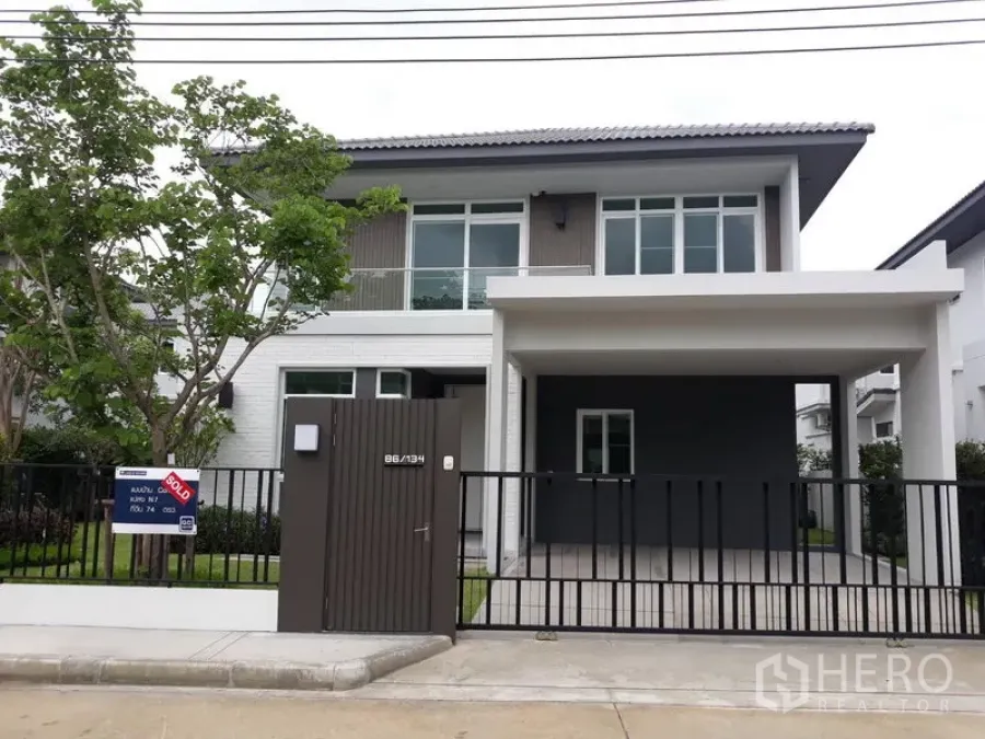Detached House for rent in Samut Prakan - Front view of a modern two-storey detached house with gated entry and covered carport.