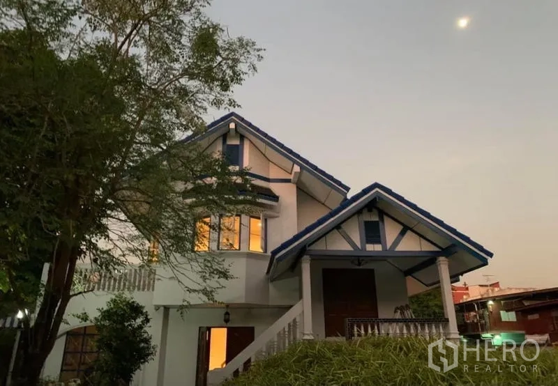 บ้าน ให้เช่าในKhlong San, Bangkok - บ้านเดี่ยวสองชั้นหลังคาจั่วสีน้ำเงินยามเย็น ไฟภายในอบอุ่น ท่ามกลางต้นไม้ใหญ่