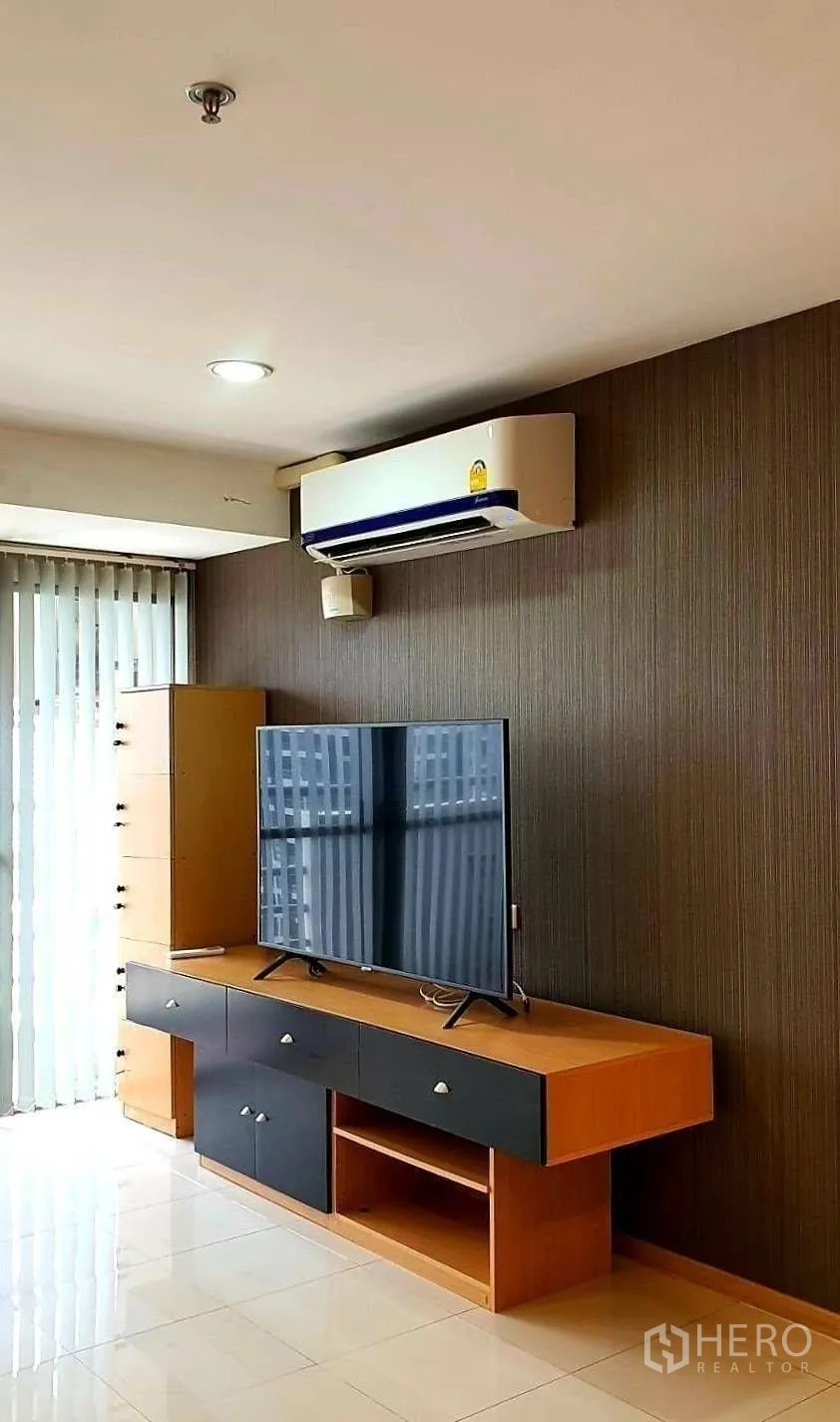 Condominium for rent in Khlong Toei, Bangkok - Corner of living room showing TV console, wall-mounted air conditioner and blinds.