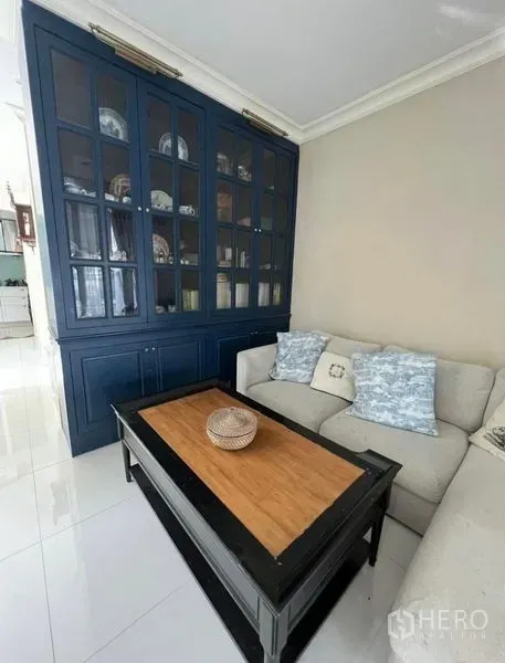 Townhouse for rent or sale in Bueng Kum, Bangkok - Bright living room with L-shaped sofa, navy built-in display cabinet, and glossy floor tiles.