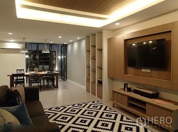 Townhouse for rent in Watthana, Bangkok - Open-plan living and dining with built-in TV wall, shelving, and sofa.