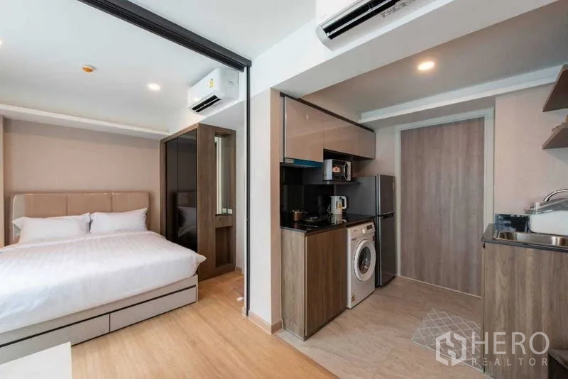 Condominium for rent in Huai Khwang, Bangkok - Bedroom adjacent to a compact kitchen with fridge, microwave and washer.