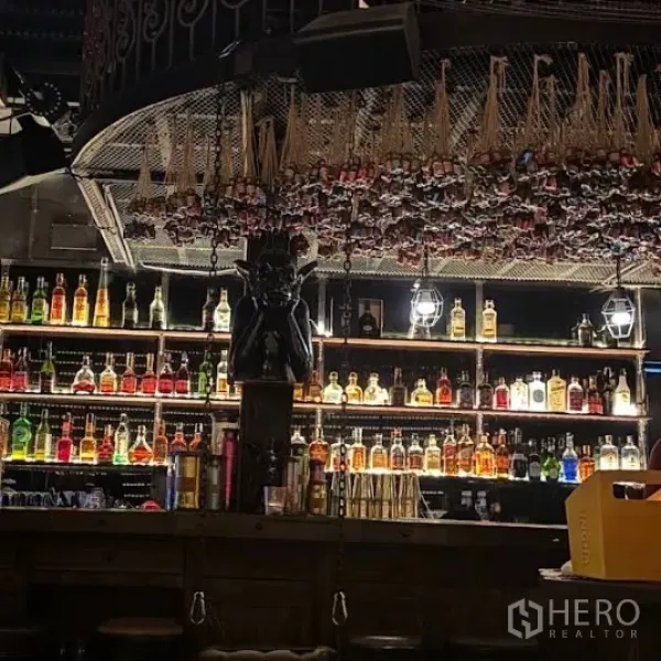 零售空间 出租在Watthana, Bangkok - 昏暗氛围的吧台，背光酒瓶陈列架与装饰性天花设计。