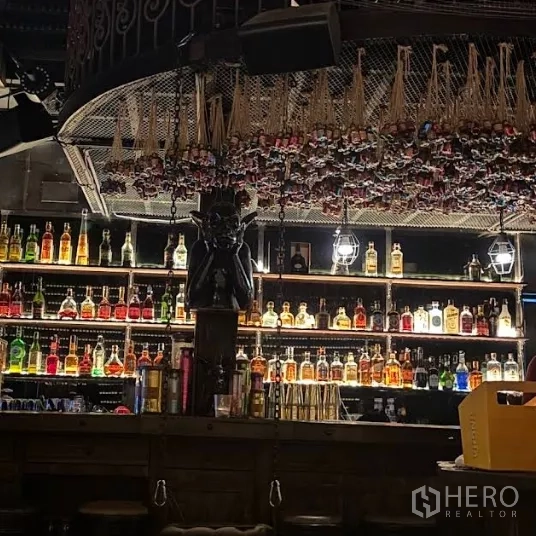 零售空间 出租在Watthana, Bangkok - 昏暗氛围的吧台，背光酒瓶陈列架与装饰性天花设计。