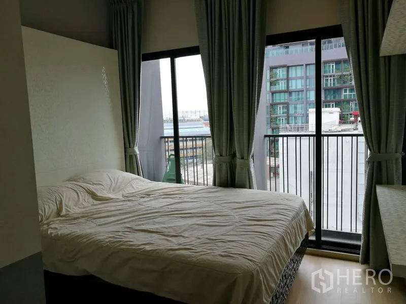 Condominium for rent in Watthana, Bangkok - Second bedroom with large windows and a balcony, city view, grey curtains and a queen bed.