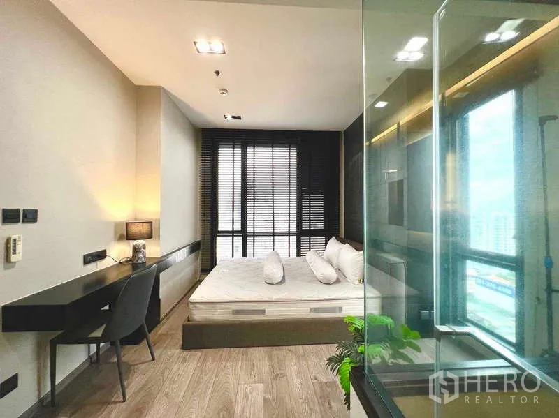 Condominium for rent - Bright bedroom with king bed, wall-to-wall windows with blinds, and a glass bathroom partition.