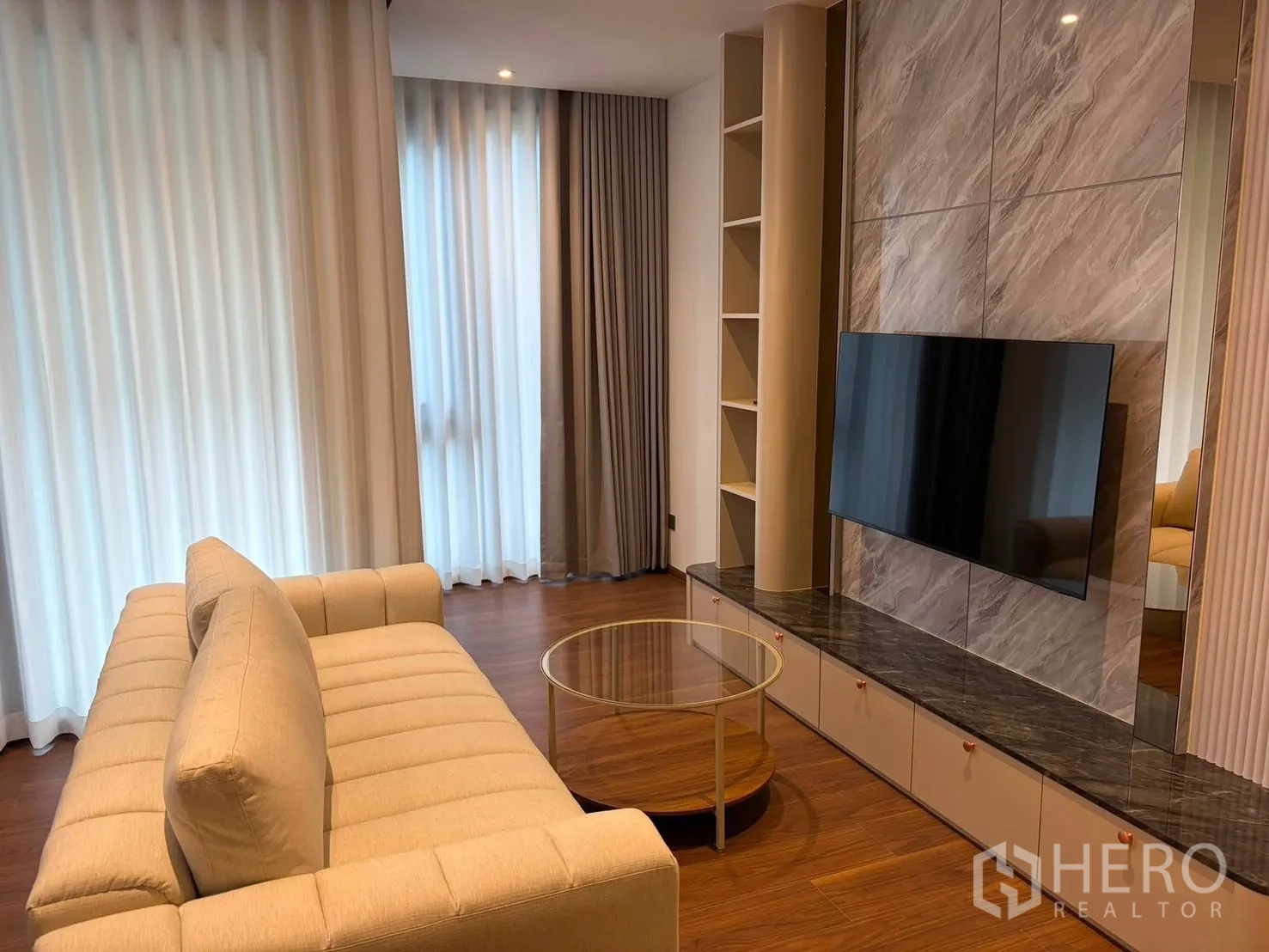 Condominium for rent in Watthana, Bangkok - Living room with beige sofa, round glass coffee table, and large windows with sheer curtains.