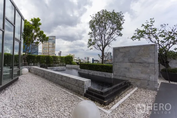 公寓 出租在Watthana, Bangkok - 屋顶花园配大理石景观水池、碎石步道与绿篱，背景为城市天际线。