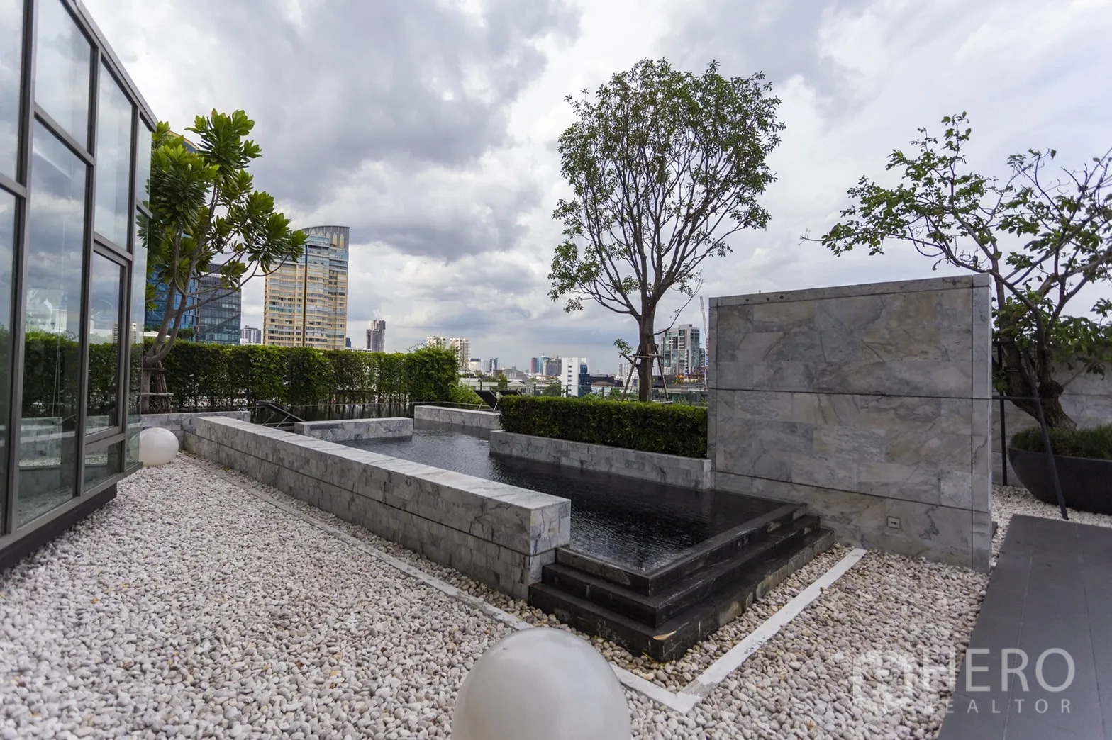 公寓 出租在Watthana, Bangkok - 屋顶花园配大理石景观水池、碎石步道与绿篱，背景为城市天际线。