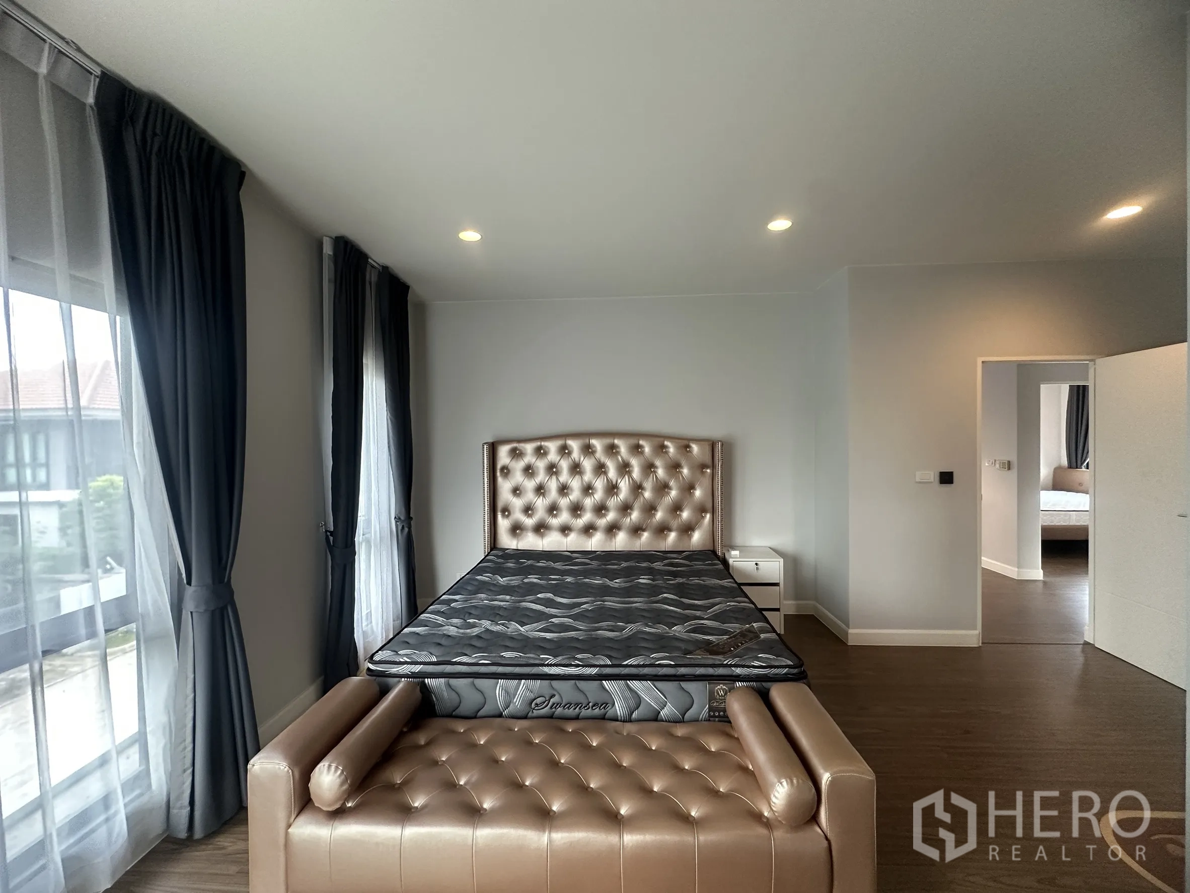 独栋房屋 for rent or sale in Lam Luk Ka, Pathum Thani - 主卧另一角度，展示软包床头、长凳与大窗帘。
