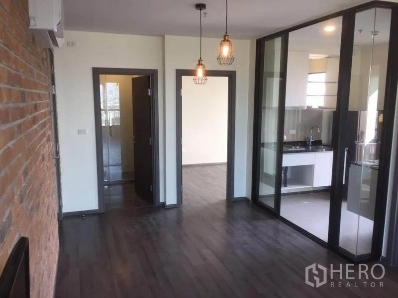 Condominium for sale in Watthana, Bangkok - Open-plan living area with pendant lights, glass-partitioned kitchen, wood floors and doors to bedrooms.