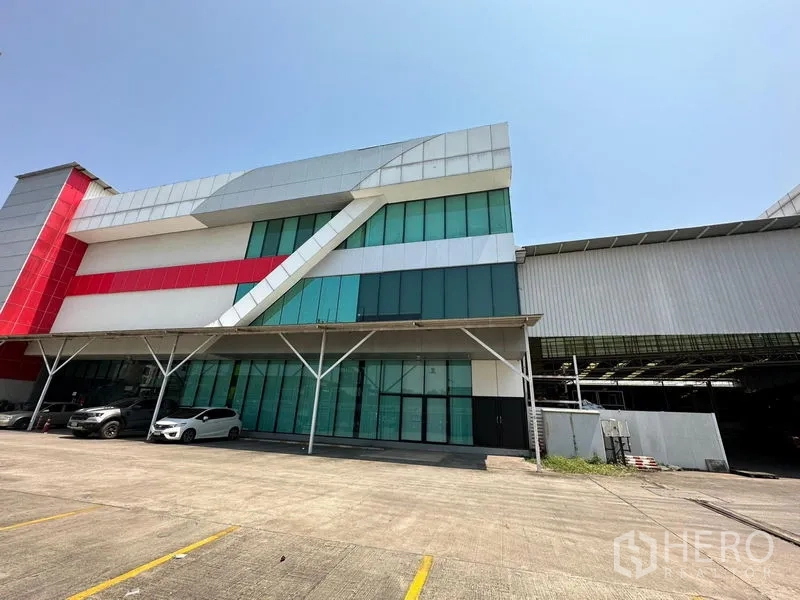 Warehouse for rent in Lam Luk Ka, Pathum Thani - Attached office building with green glass panels and a red accent next to the warehouse.